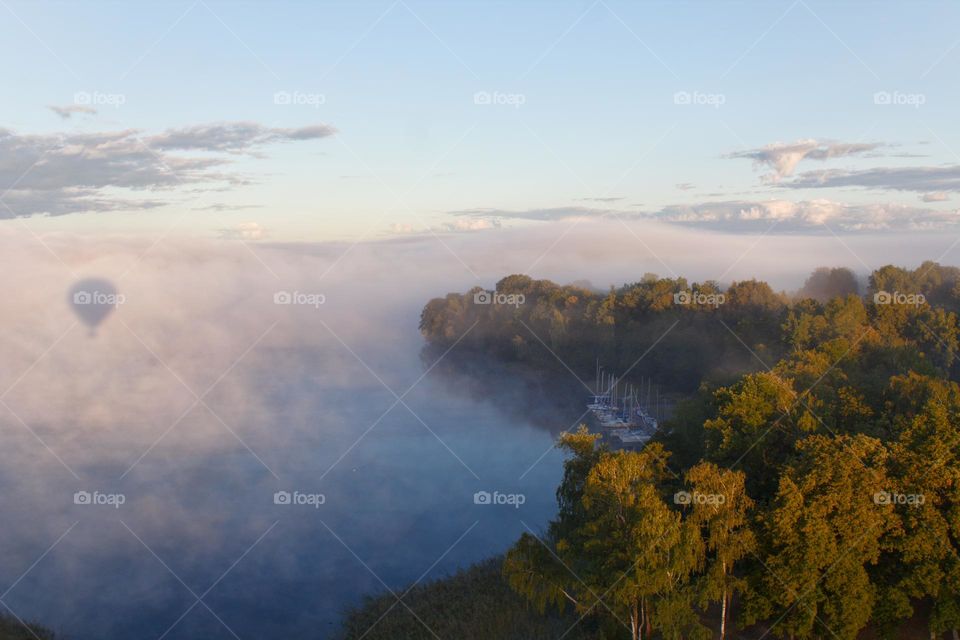 Flying balloon shadow on the clouds near Kaunas with a strand of trees.