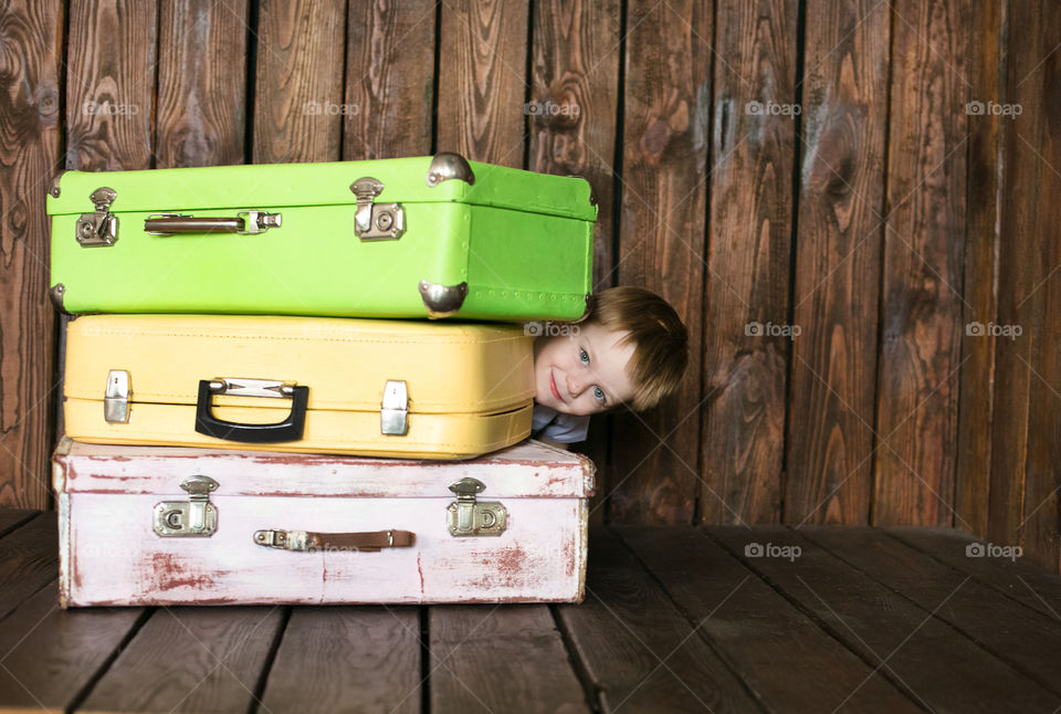 Smiling boy peeking from suitcase stack