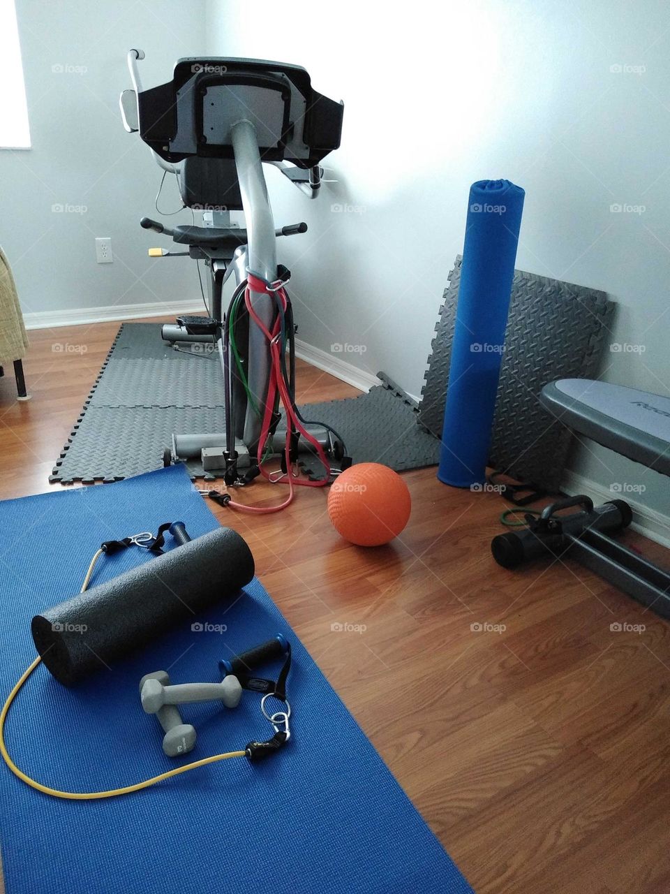 The indoor gym at a friends house that includes an exercise bike, a yoga mat with dumbells on it.