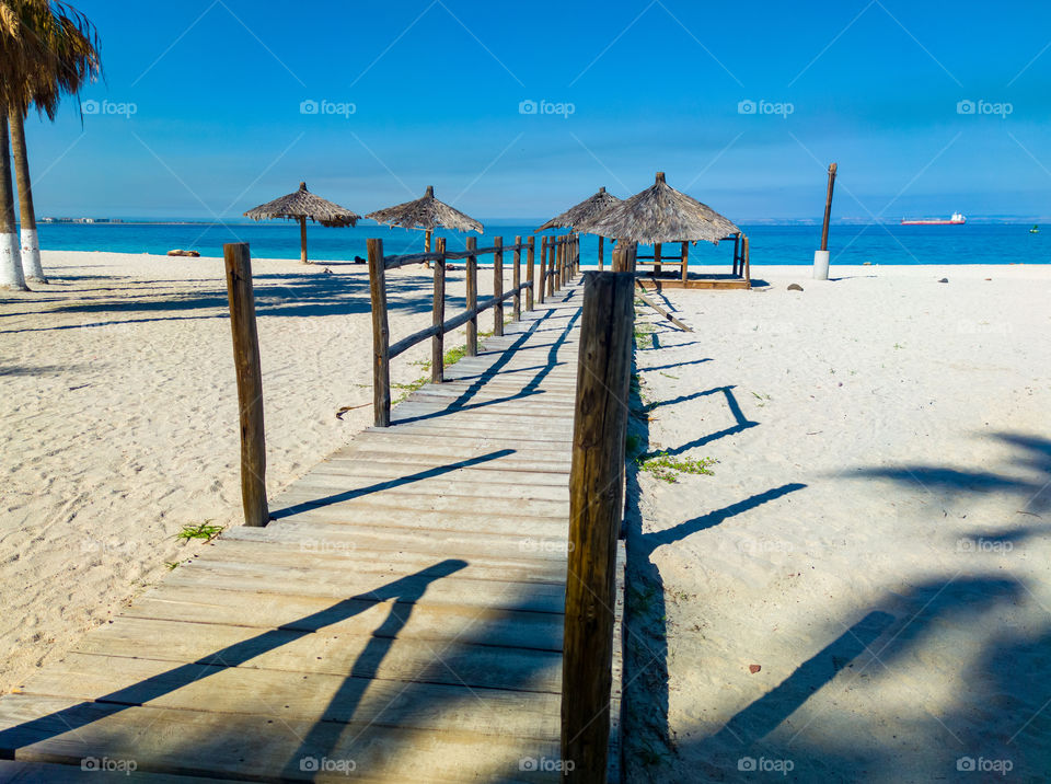 Wooden walkway on a beach with some umbrellas in the background (La Paz Mexico)