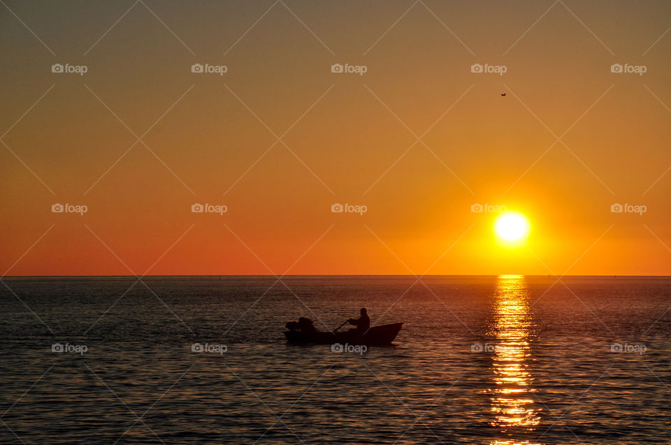 the boat with the fisherman in the sea at sunset