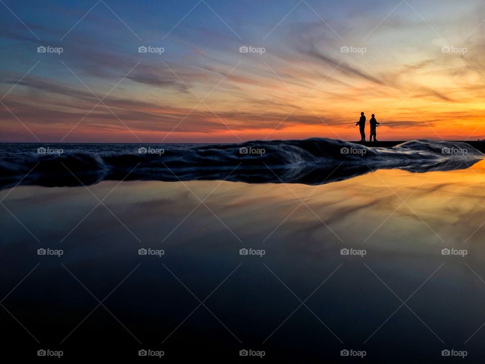 Silhouettes of two fishermen fishing on sunset. 