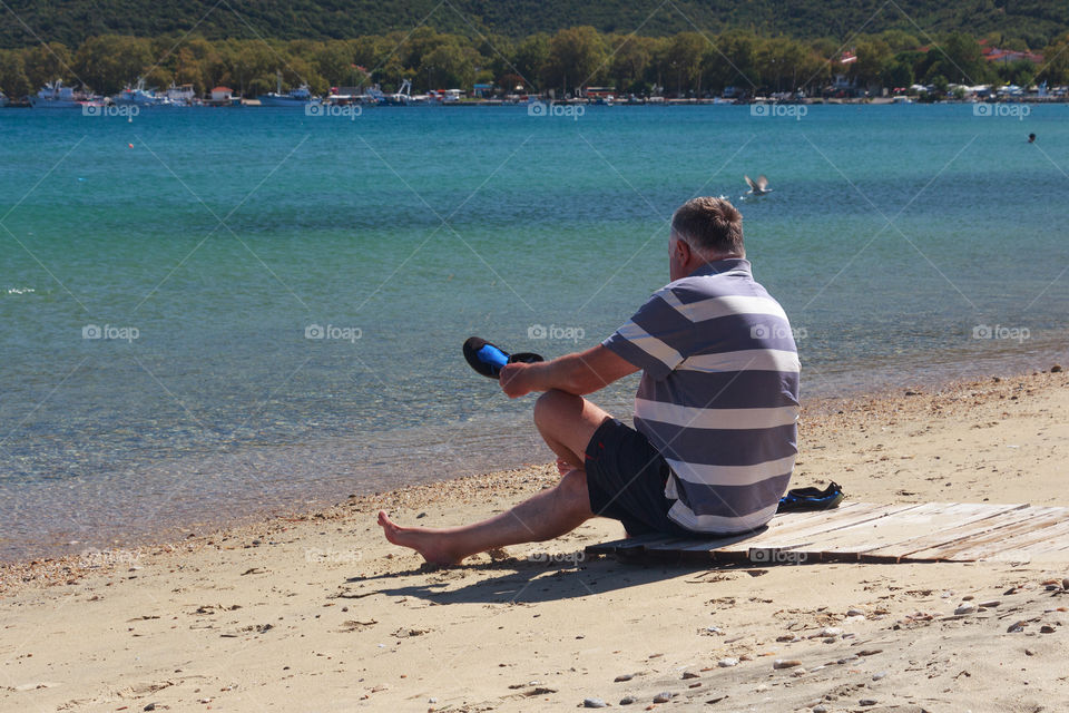 Senior man puts shoes on rocky beach in Greece