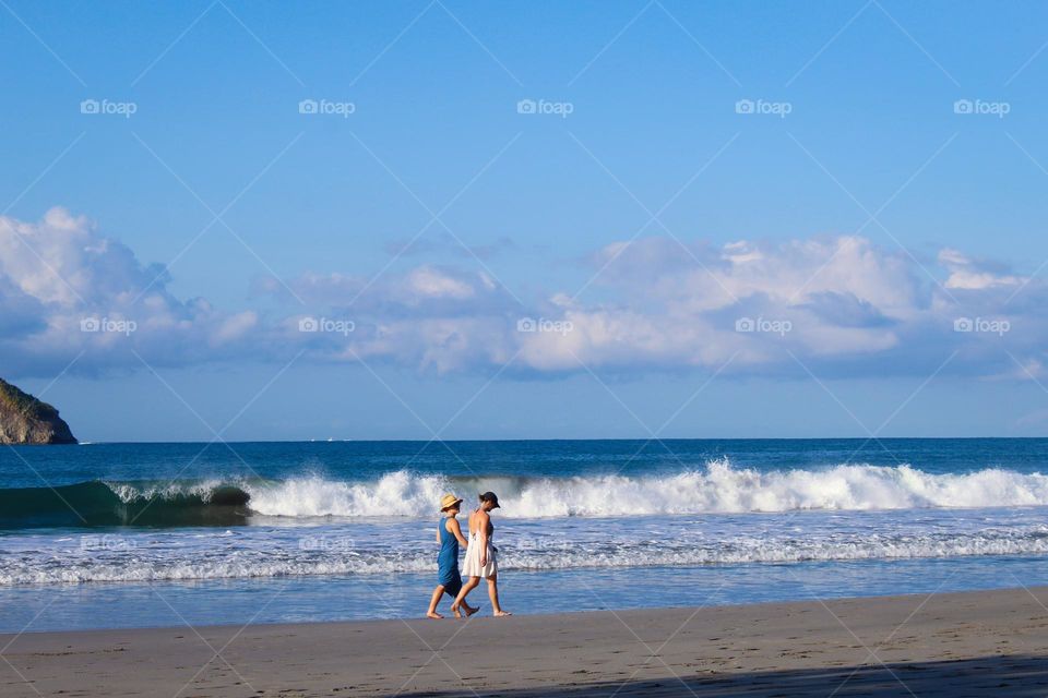 Summer landscape.  View of the girls with hats and summer dresses walking on the sandy beach