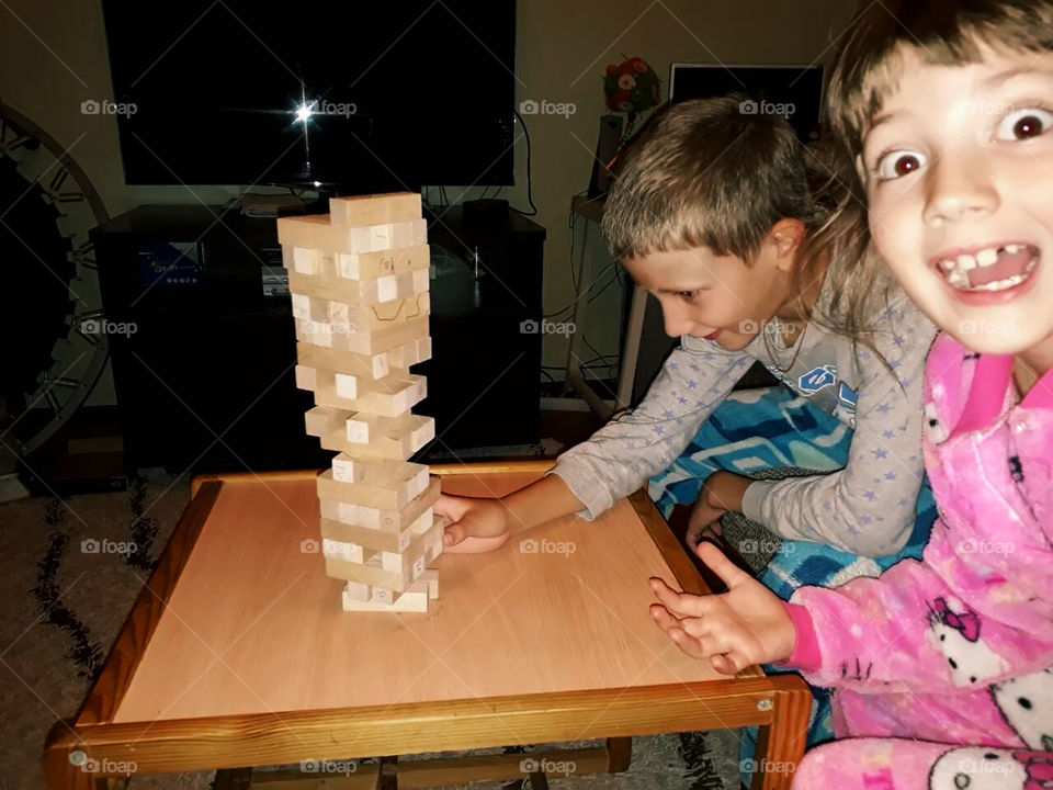 Happy kids playing jenga at home in the evening 