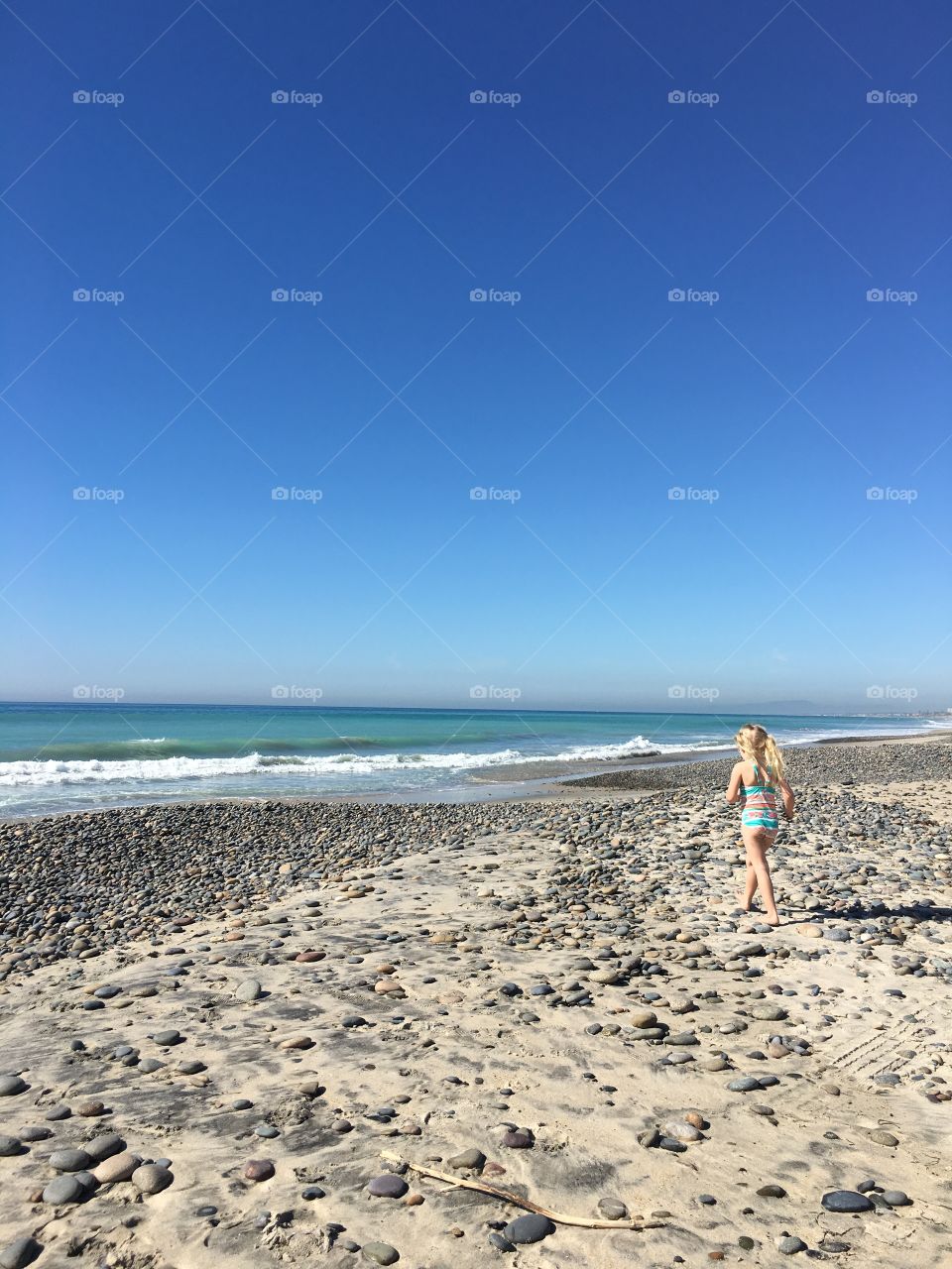 A classic style photo of a girl approaching the shoreline on a rocky beach.