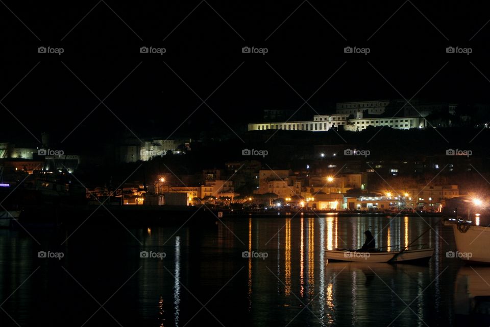 A lonely fisherman waits in front of a scenic landscape, during a cold night.