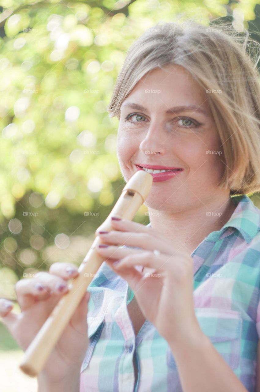 a young beautiful caucasian girl dressed in pin-up style plays the flute and smiles, bright sunny day.

