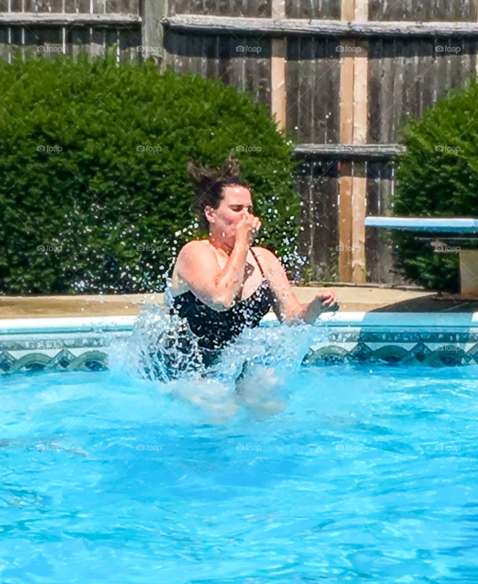 Jump!  Woman holding her nose and jumping into a swimming pool.  She makes a big splash! 