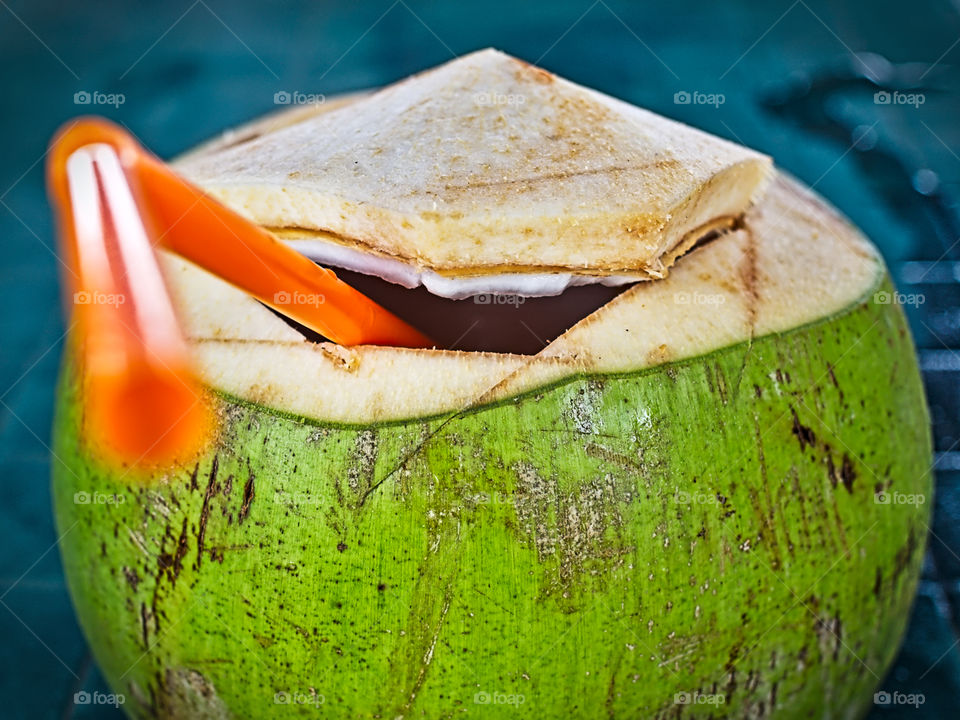 Isolated green young coconut cut at the top with straw inserted inside and white meat partly showing