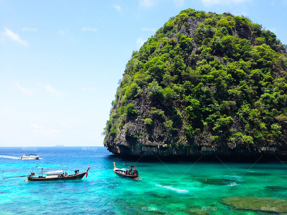 Boats swimming at the green tropical island in the turquoise sea water in Thailand 