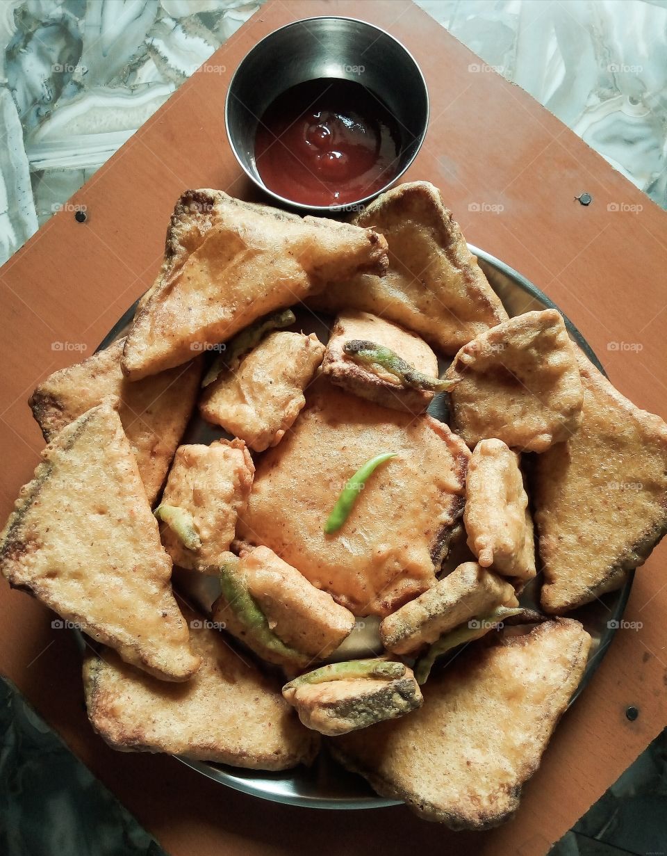 Bread Pakora is an Indian fried snack (pakora or fritter) served with sauce. ​A common street food, it is made from bread slices, gram flour, and spices among other ingredients.