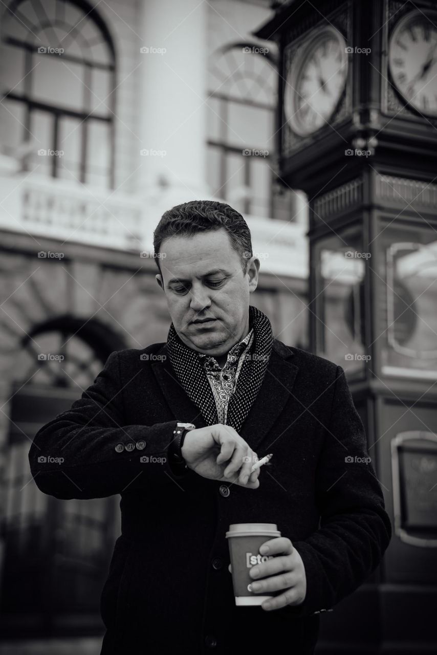 Black and white photo portrait of a man waiting for a meeting in the city square under the clock