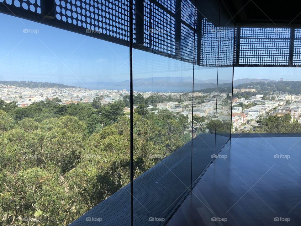 A top floor view of a sunny day at a museum looking out at the city below and the bay and hills in the background 