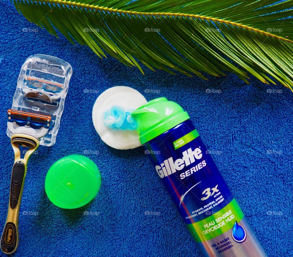 Gillette shaving cream and razor on a blue towel with palm leaf.