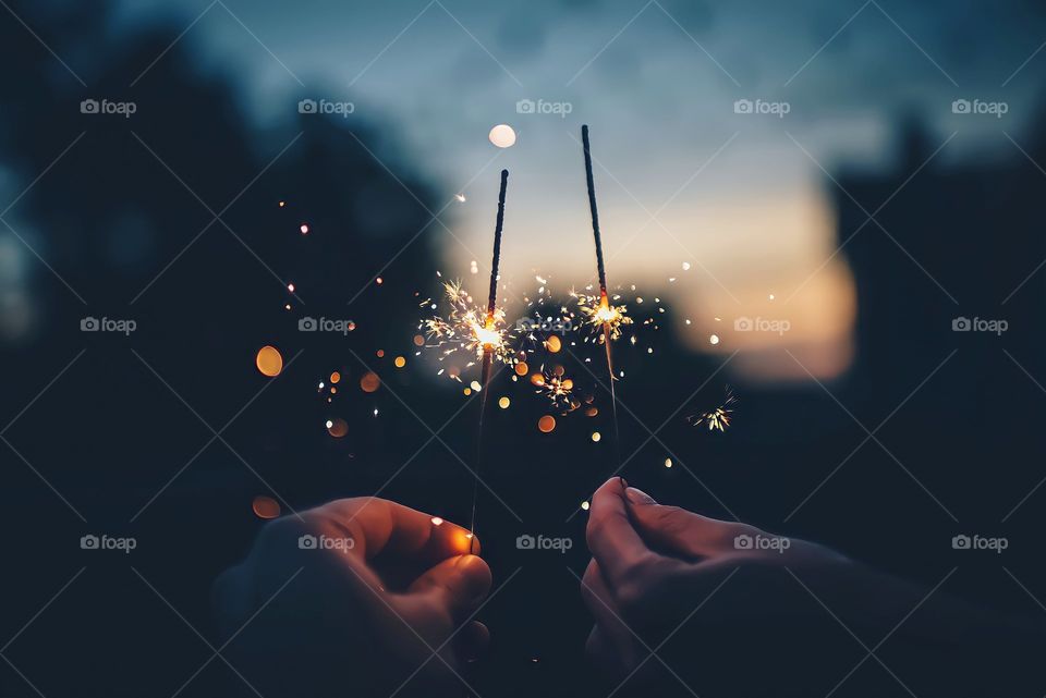 Two Sparklers
Close up of two hands holding burning sparklers during night time.