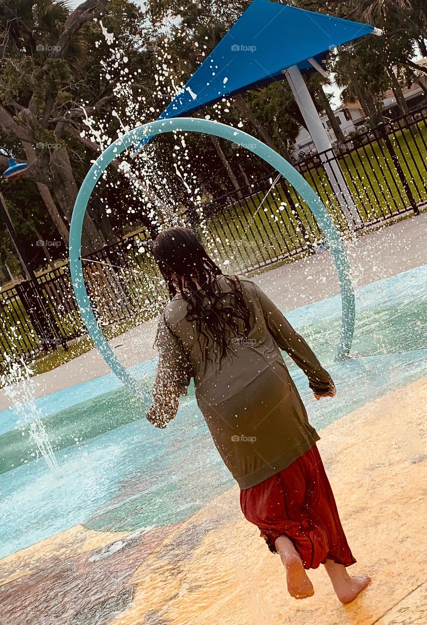 Children having lots of fun in the water at the colorful kids splash pad at the city park for children during a really warm day in Florida.