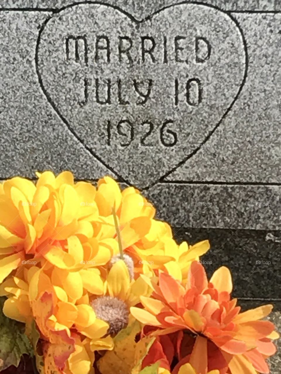 Headstone with engraved marriage date and artificial flowers in the forefront.