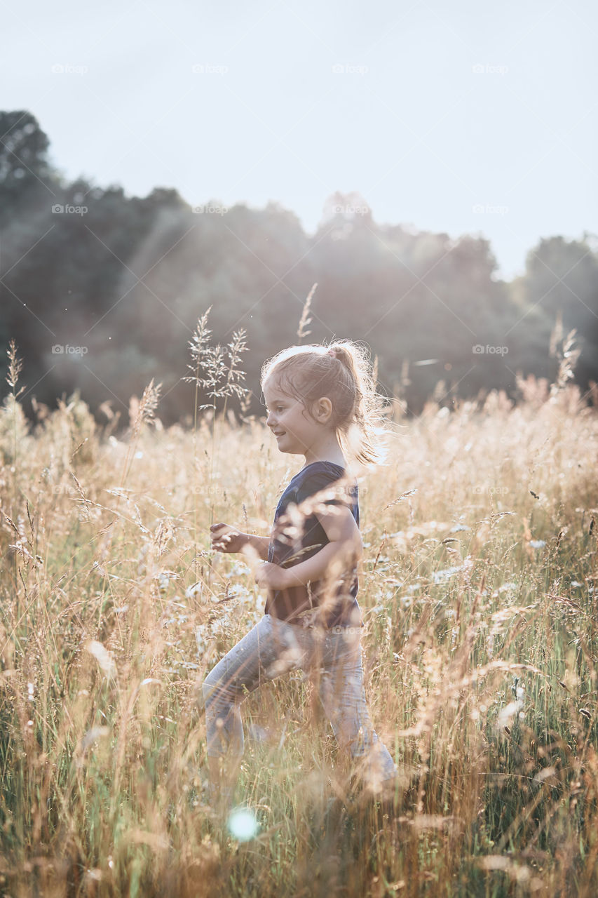 Little happy girl walking through a tall grass in the countryside. Candid people, real moments, authentic situations