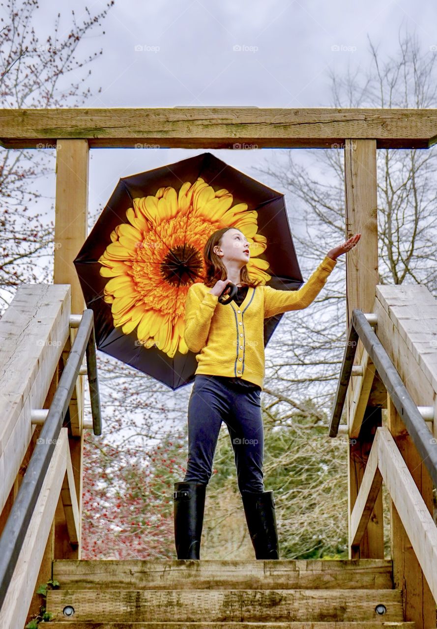 Girl under big flower umbrella checks for rain 