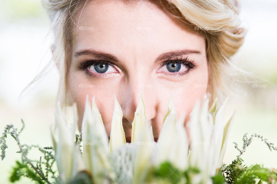 2019 photos - portrait of woman's blue eyes behind a white king protea