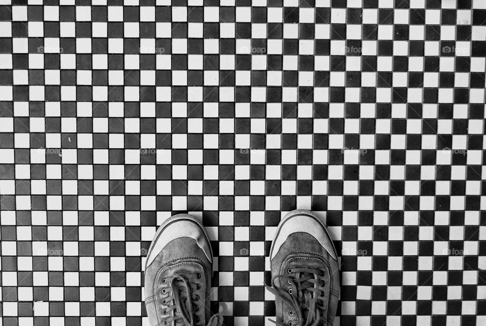 Looking down onto a pair of shoes that are standing on a chequer board, black and white checked floor.