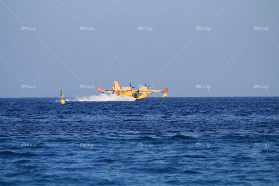 A canadair and a helicopter collect water and fly to the mountains to put out a big fire in Liguria.