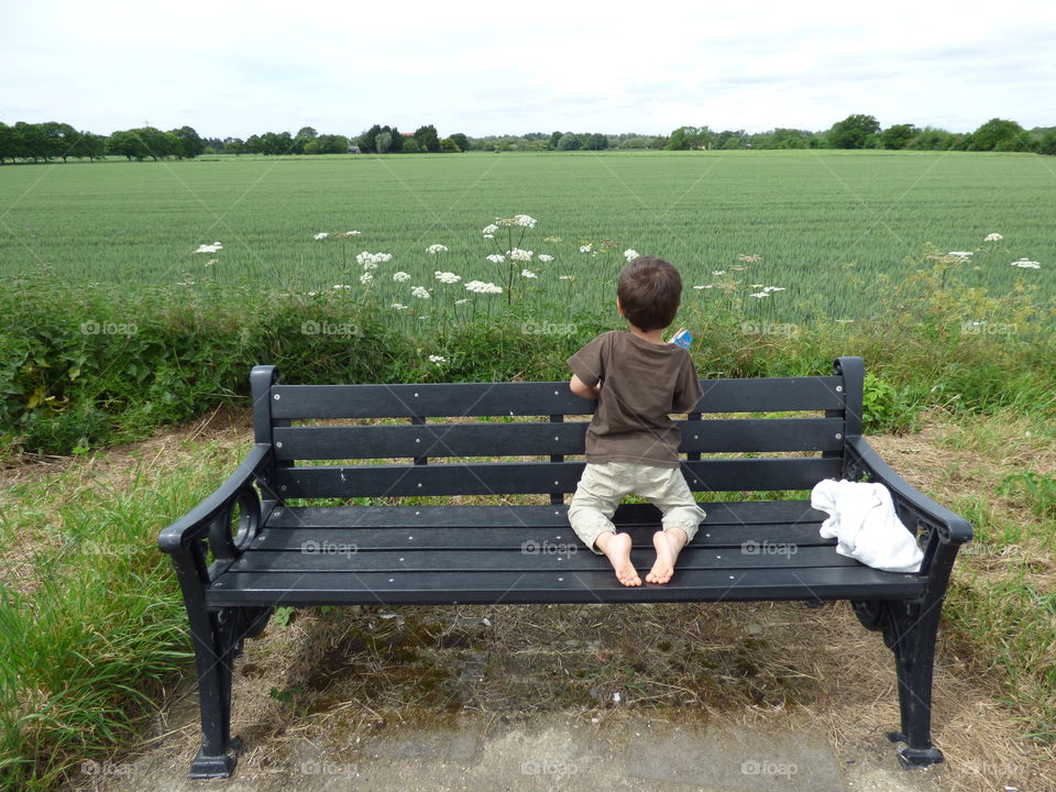 little boy curiously looking at the rye field in the distance sitting on his knees bare feet looking back in a lovely spring day