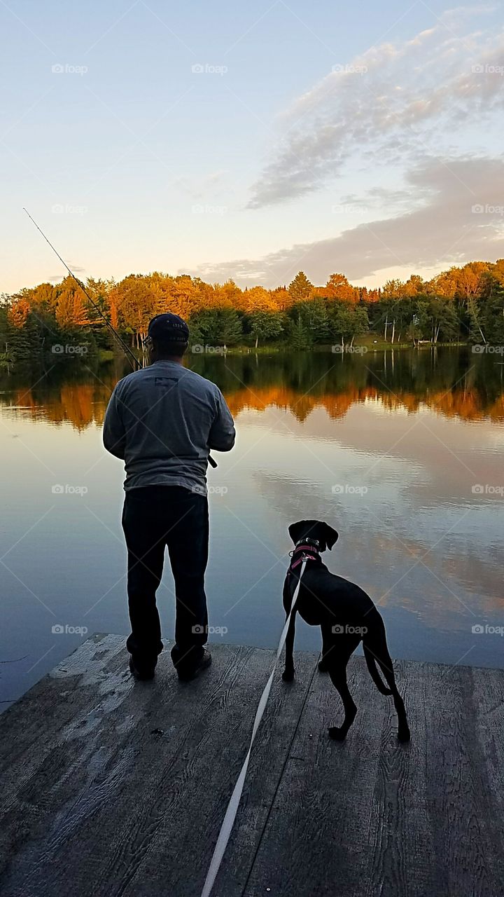 a man fishing with his dog at sunset