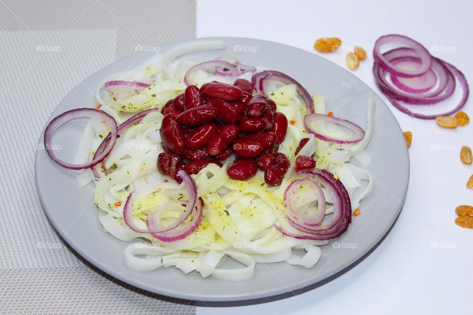 Rice noodles with red beans and purple onions on gray plate . Angle view of food