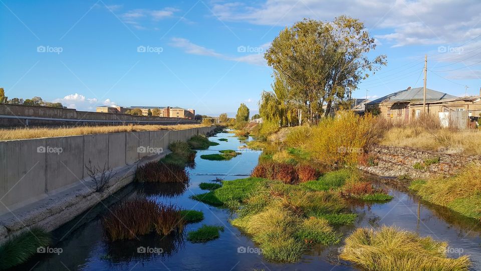 blue calm and beautiful river that flows through the village, the river has beautiful green and yellow grass, and on the Bank of trees, beautiful autumn view