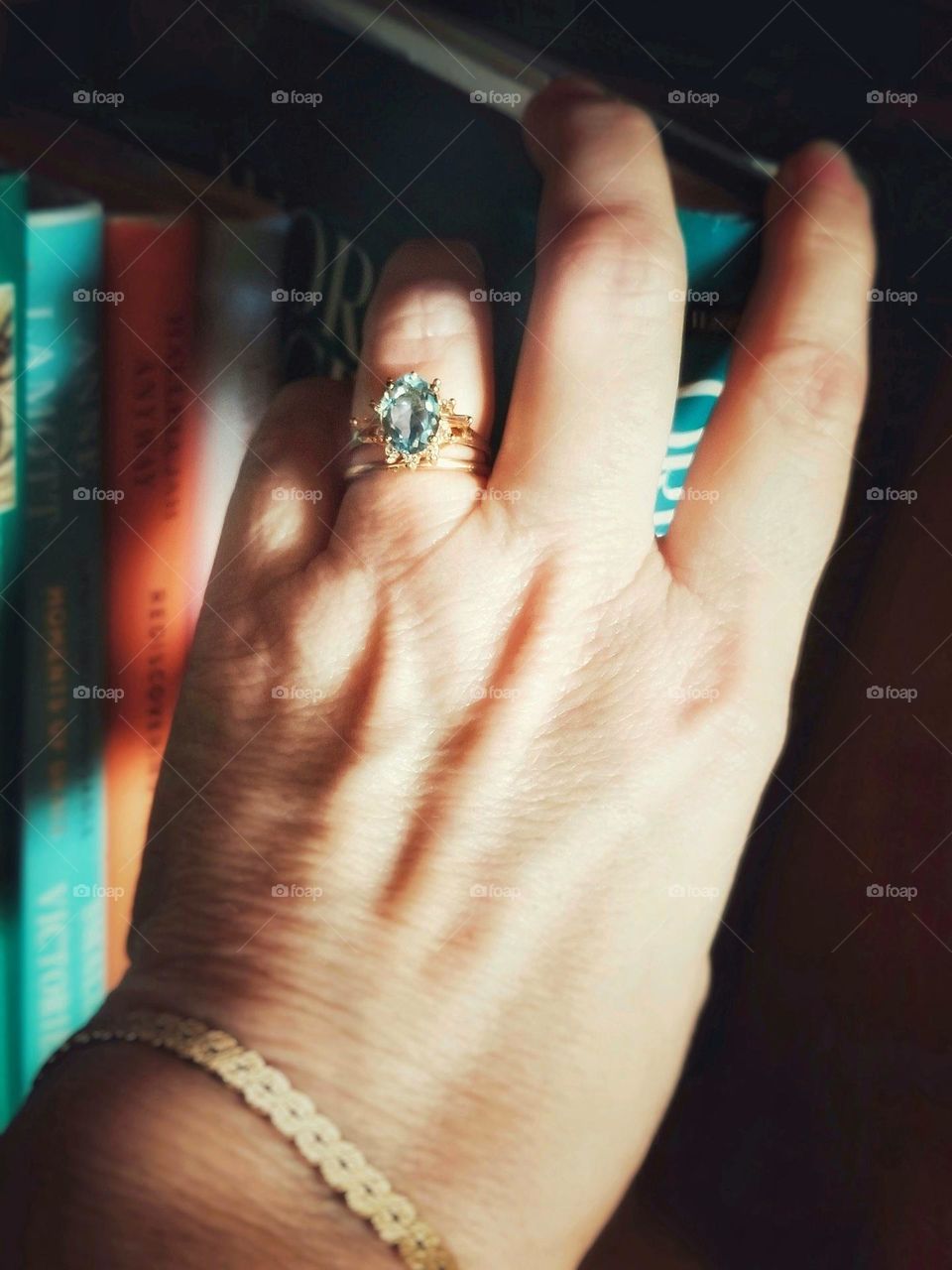 Aquamarine Ring & gold bracelet being worn by a woman reaching for a book off a shelf