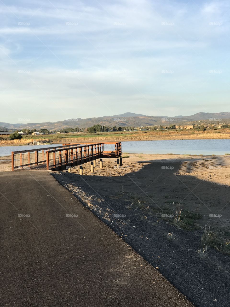 A wooden viewing bridge extends to a pond in a wildlife park outside of Prineville in Crook County in Central Oregon with the golden glow of evening on a fall day. 