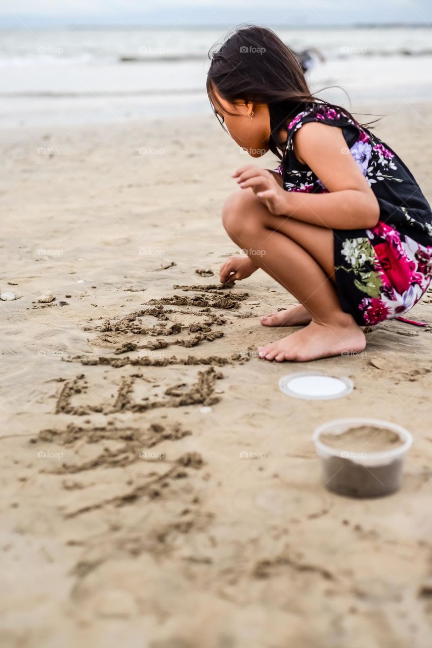 An Asian girl writing on the sand on the beach