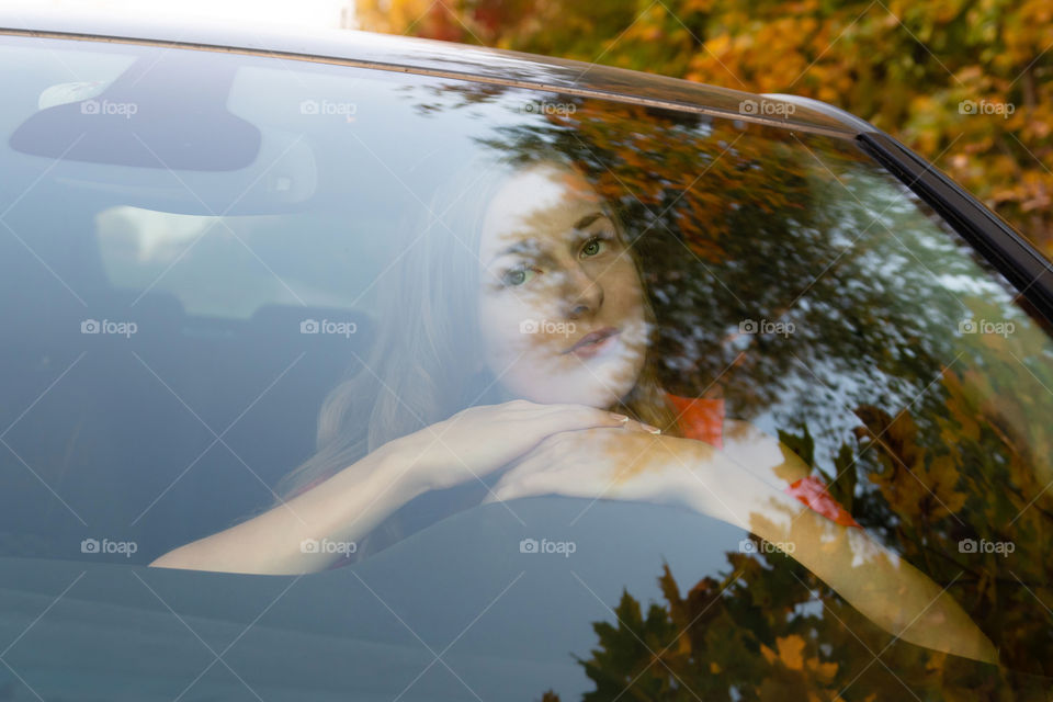 a young beautiful woman with long hair sits at the wheel of the car and dreamingly watched through the glare of the front windshield