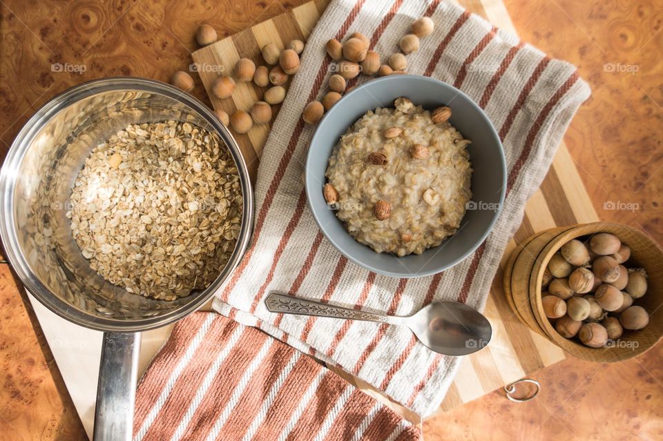 Cooked oatmeal in a deep gray plate with hazelnuts and honey.