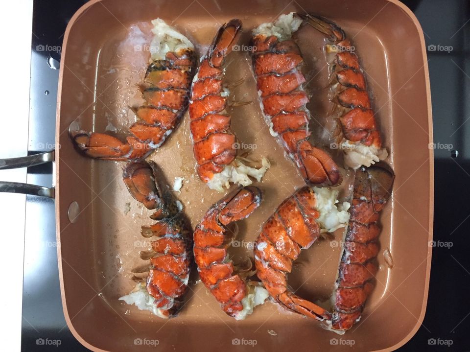 Lobster tails pan fried in butter in a copper pan on the ceramic top stove for dinner