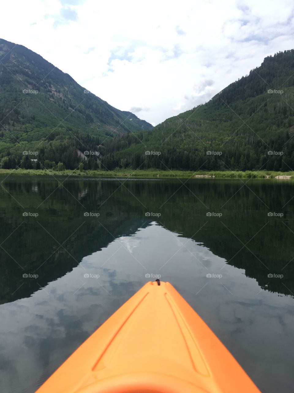Kayaking on a calm mountain lake repeating shapes of the kayak, reflection in the water & mountain valley to add interest.