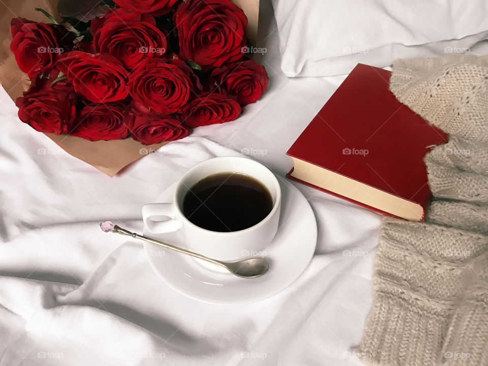 Coffee cup, red book and red roses in white bed 