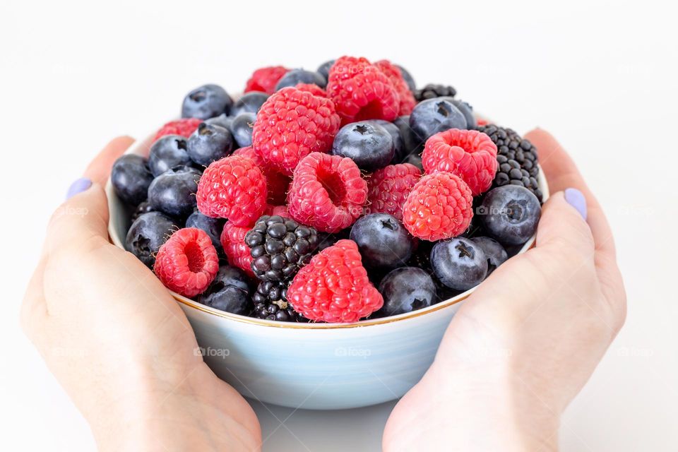 Fresh organic berries in a bowl in hands, healthy summer food