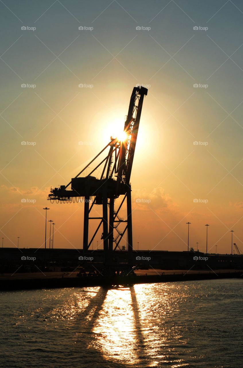 A towering industrial crane stands in perfect silhouette off the Savannah river of Georgia.