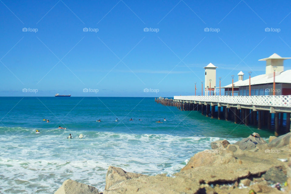 Pier on the beach with surfers and ship on the horizon