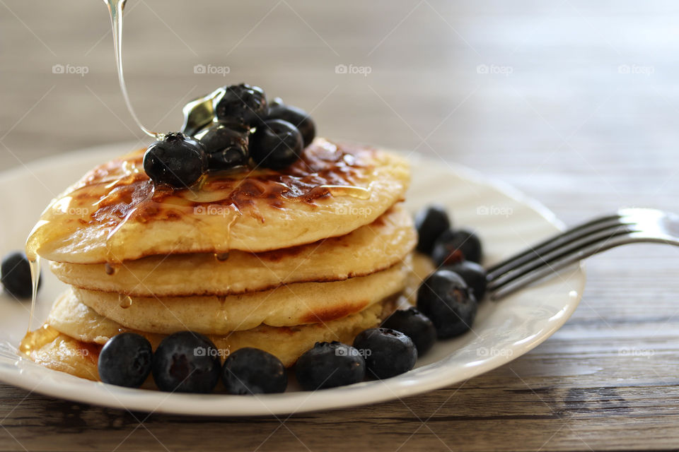 Freshly made golden pancakes with honey and blueberries on a plate