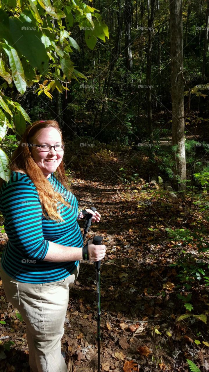 Well built redhead with glasses pauses on a hike with trekking poles through a state park in Georgia.