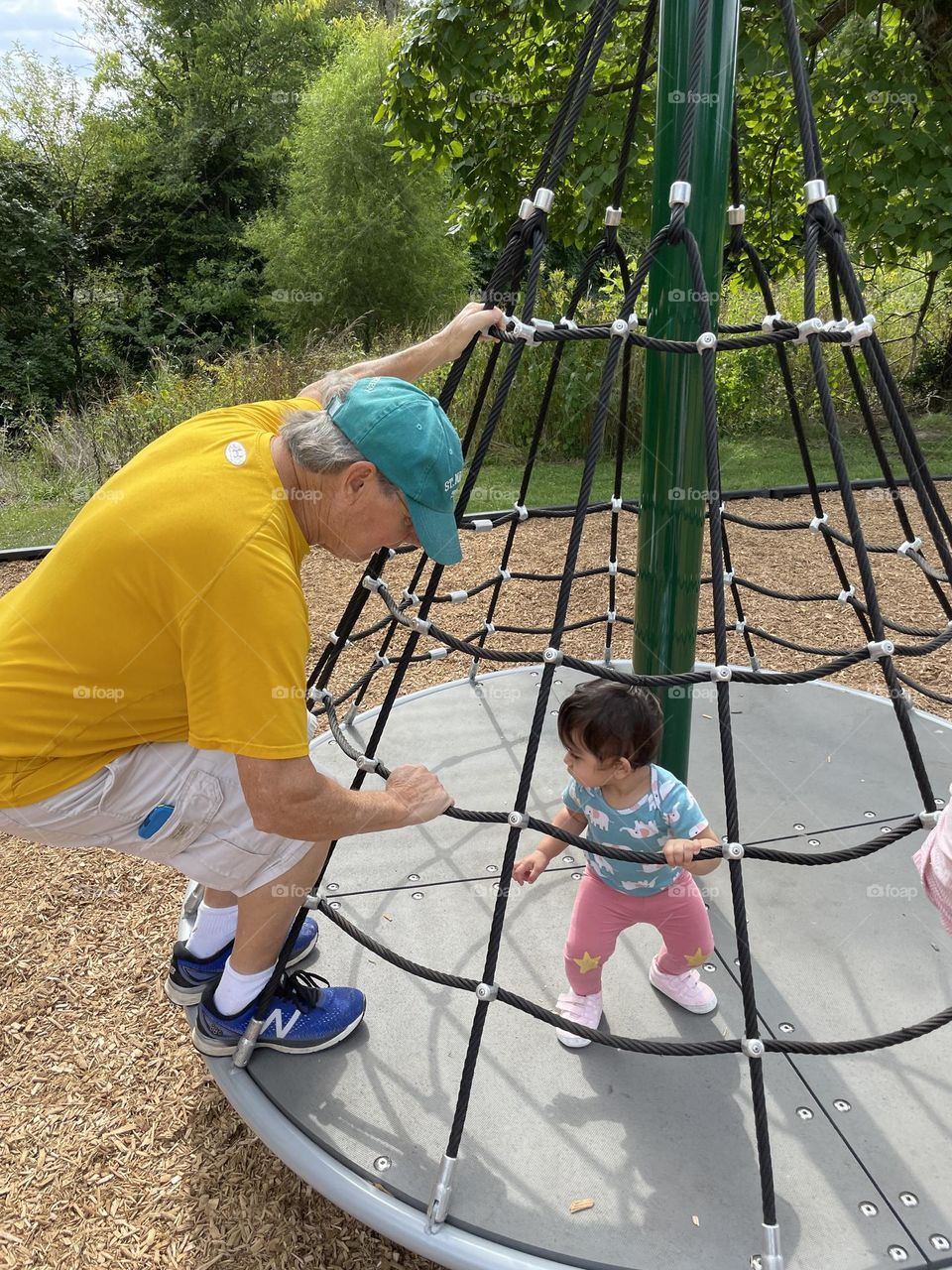 Grandfather and baby riding on merry go round, grandpa and grandchild playing on playground in the summertime, summer fun on the playground, spending time with grandpa