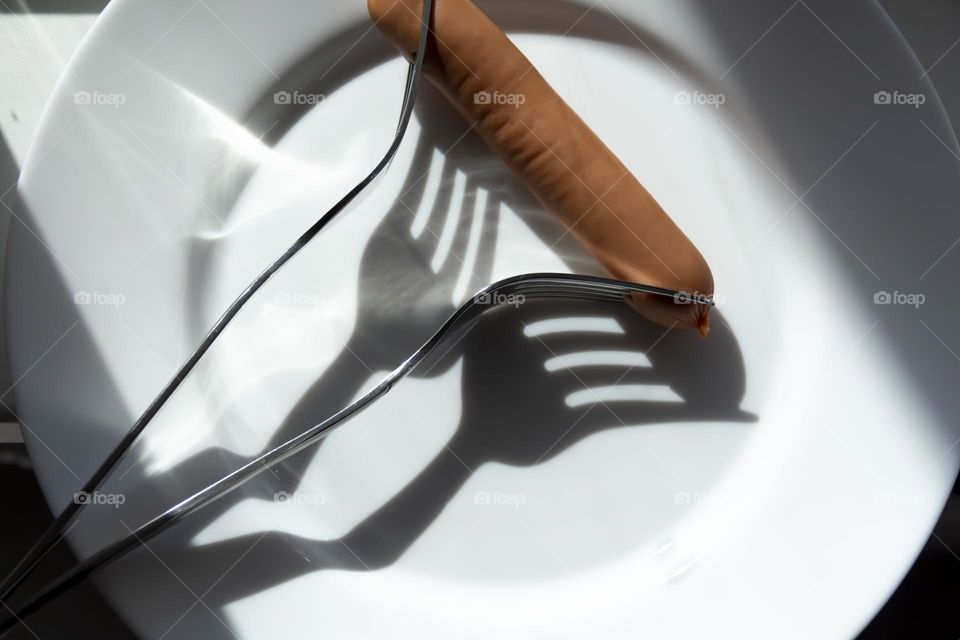 One sausage and two forks on a white porcelain plate.