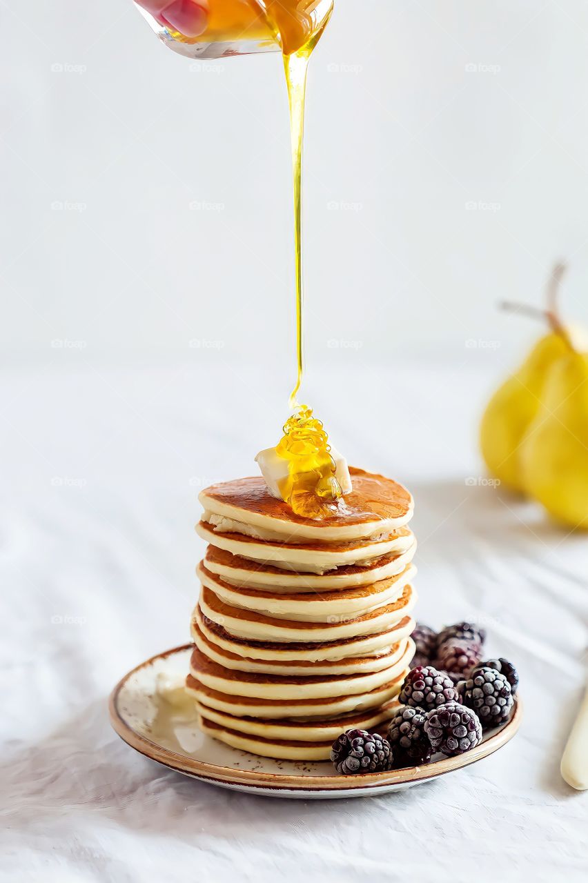 Honey being poured on pancakes
Honey being poured on a stack of pancakes alongside frozen blackberries on blurred background.