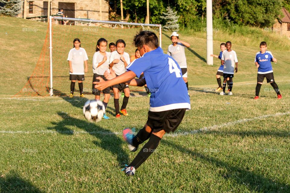 Boy is kicking the ball while another team is trying to protect their net, fear on the faces