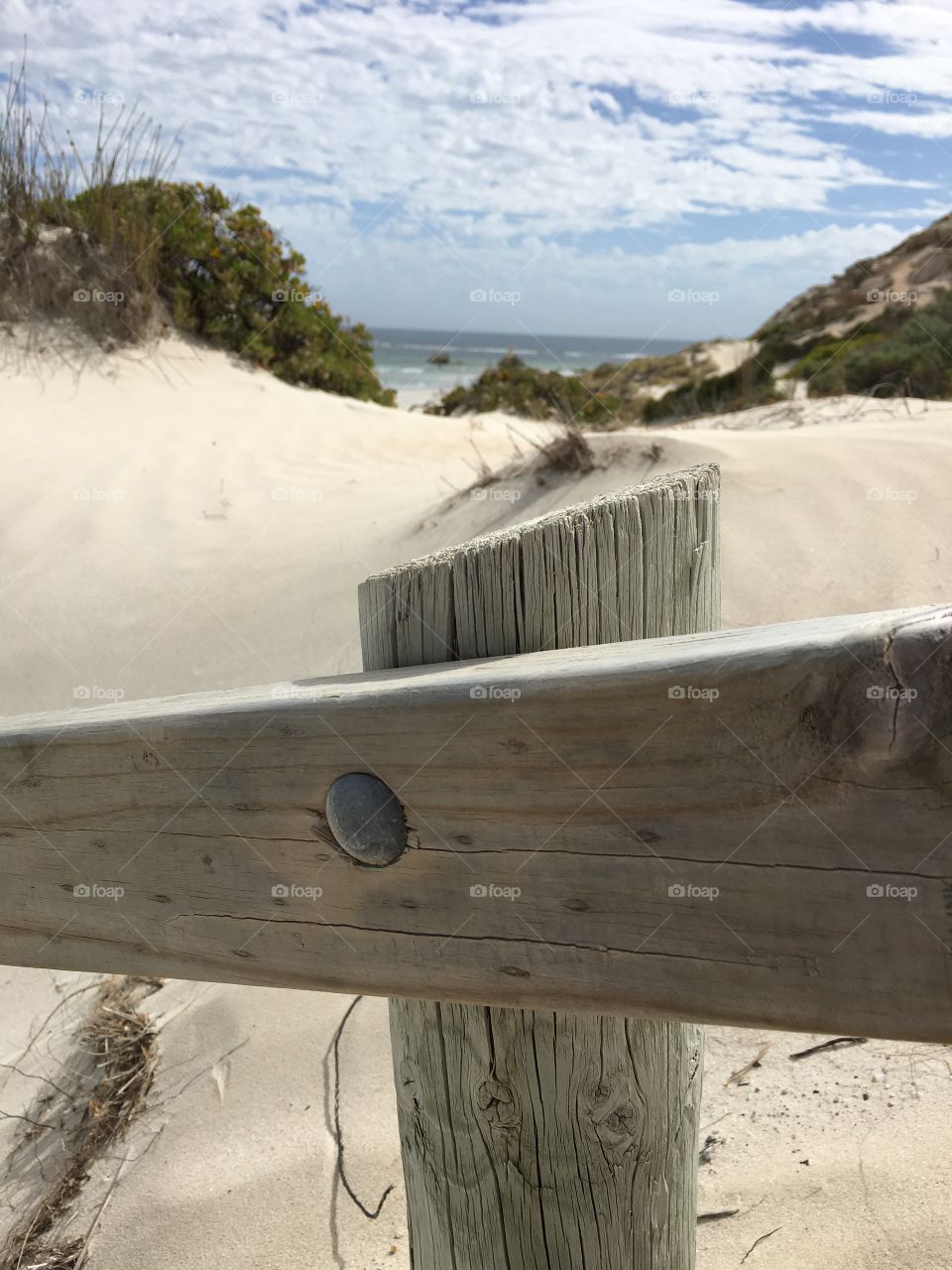 View of path to secluded remote beach from perspective of weathered wood handrail. 