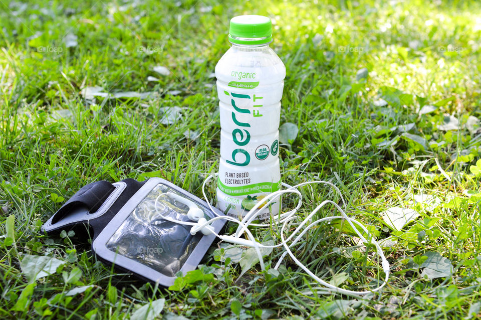 Bottle of Berri Fit in the grass next to an arm band and headphones